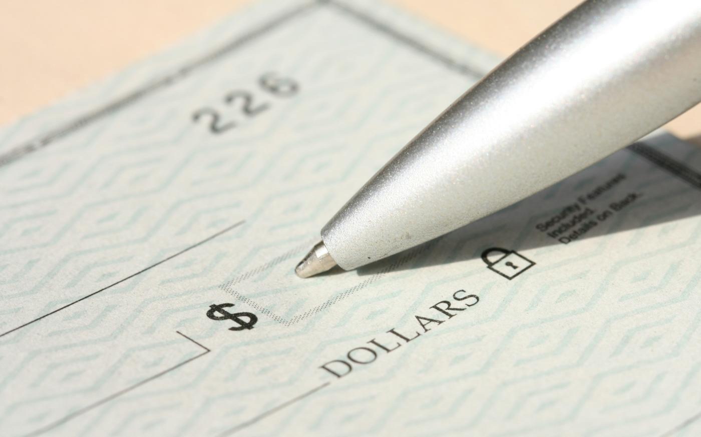Pen poised over a check, ready to write. by Money Knack courtesy of Unsplash.