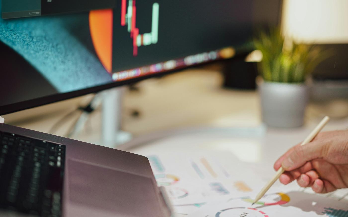 a person writing on a piece of paper next to a computer monitor by Jakub Żerdzicki courtesy of Unsplash.