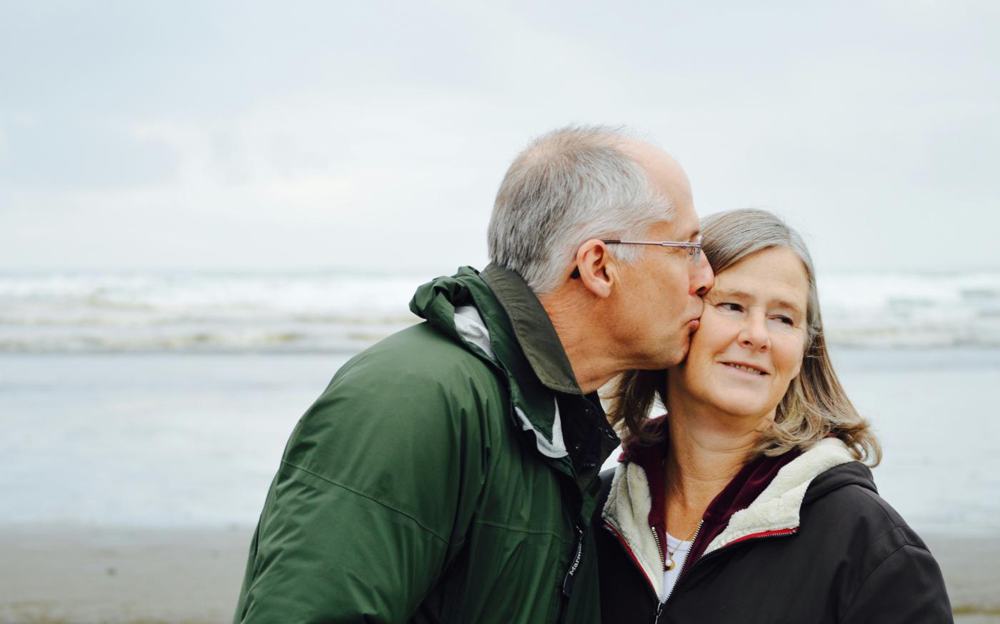 man kissing woman on check beside body of water by Esther Ann courtesy of Unsplash.