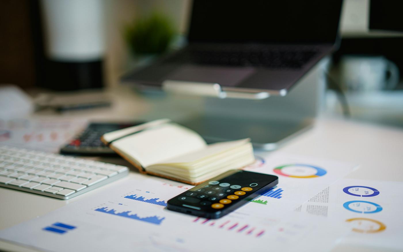 office desk with smartphone and financial charts by Jakub Żerdzicki courtesy of Unsplash.