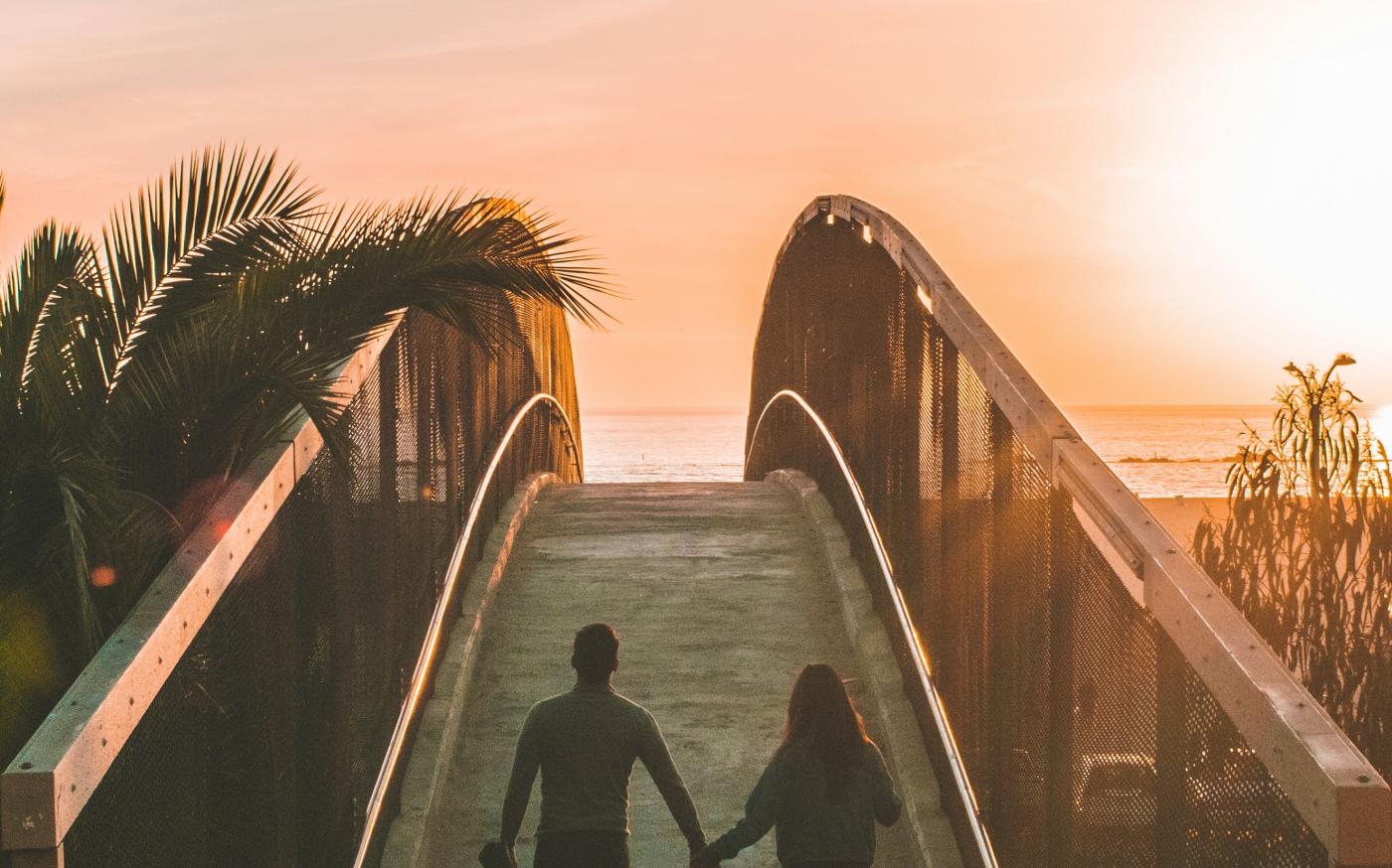 man and woman holding hand while walking on bridge by Shea Rouda courtesy of Unsplash.