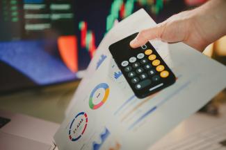 a person holding a calculator over a piece of paper by Jakub Żerdzicki courtesy of Unsplash.
