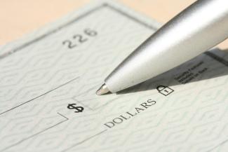 Pen poised over a check, ready to write. by Money Knack courtesy of Unsplash.