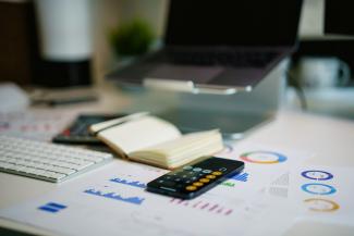 office desk with smartphone and financial charts by Jakub Żerdzicki courtesy of Unsplash.